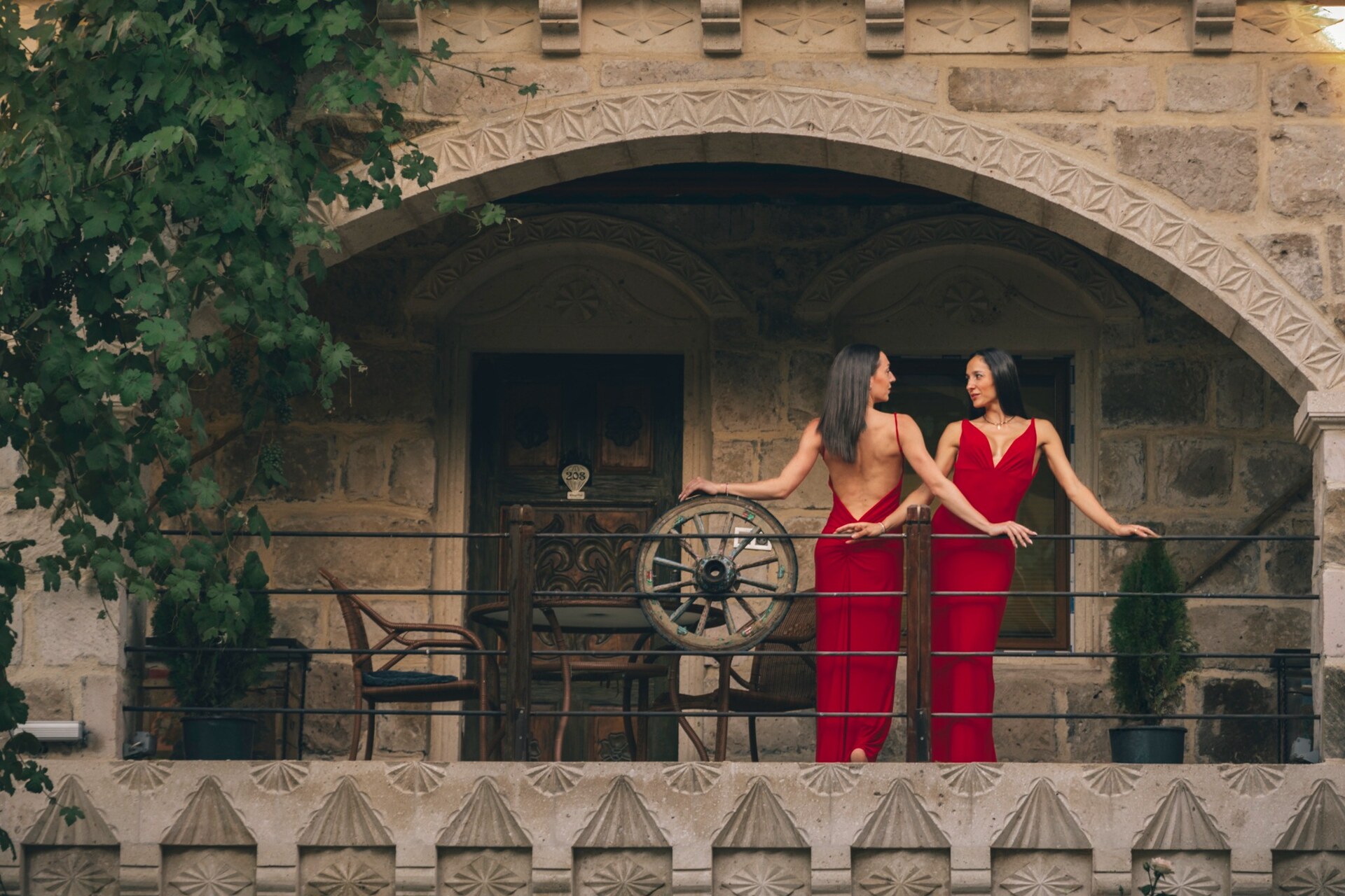 Taş otel balkonunda kırmızı elbiseli iki model ile lifestyle çekimi